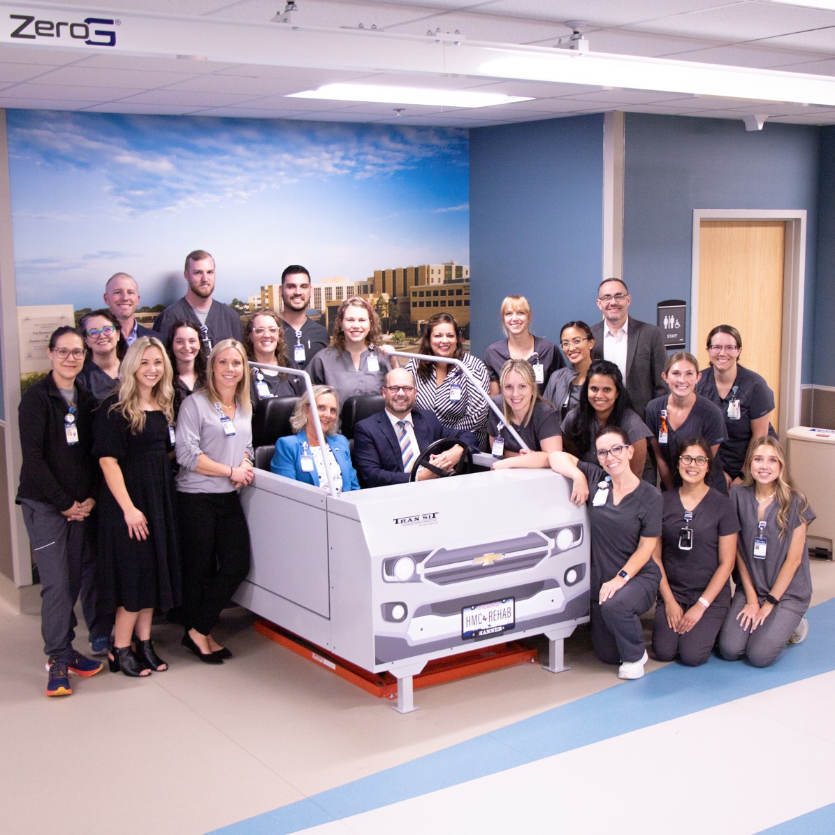Group photo of staff of Hendrick Rehabilitation Hospital around vehicle transfer simulator