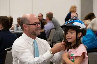 Photo of Mr. Holland helping student put on bike helmet.