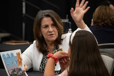 Color pic of woman with raised hand talking with student